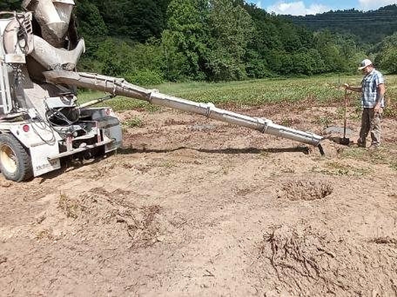 A concrete truck chute pouring onto a prepared site in an open field